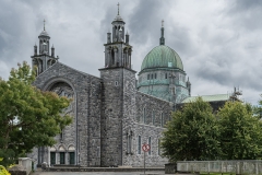 Galway, Ireland - August 5, 2017: Outside view of the Cathedral with green dome, main entrance at nave flanked by two towers. Street scene with green trees on sides.